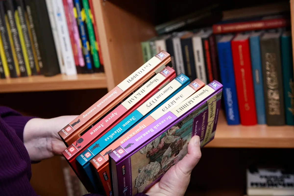 Детские книги в руках волонтёра на фоне библиотечных полок